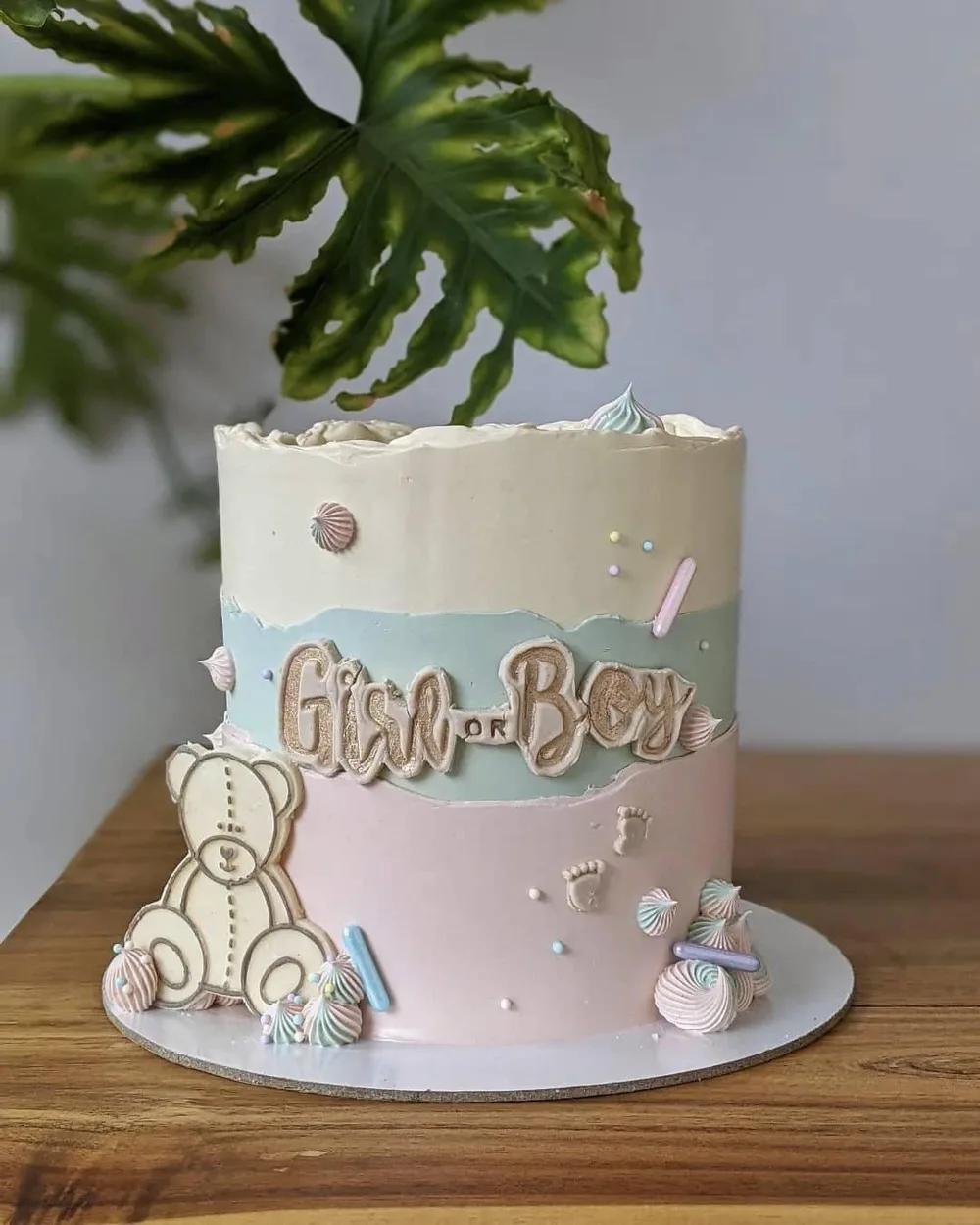 gender reveal cake in pink, blue and cream with a teddy bear and baby-themed decorations