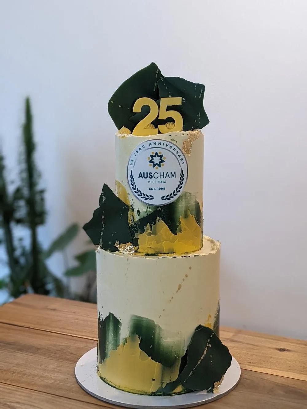 two-tier corporate anniversary cake with green and gold brushstrokes and a printed logo