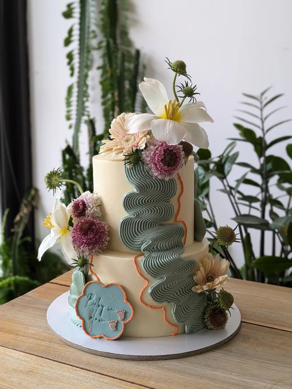 two-tier ivory cake with sage green piped waves and fresh flowers