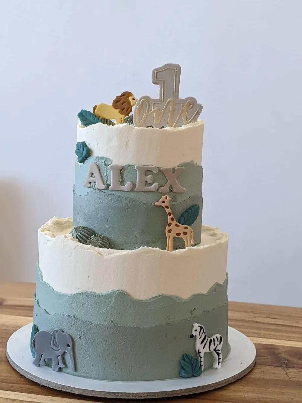 two-tier safari cake in blue-grey and cream with giraffe, lion, elephant and zebra cookies