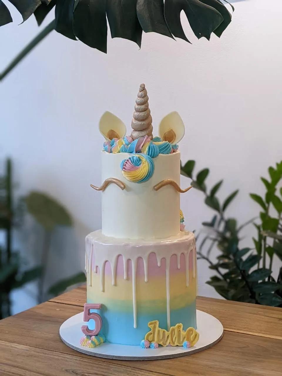 two-tier unicorn cake with a gold horn, rainbow mane and pastel ombre drip